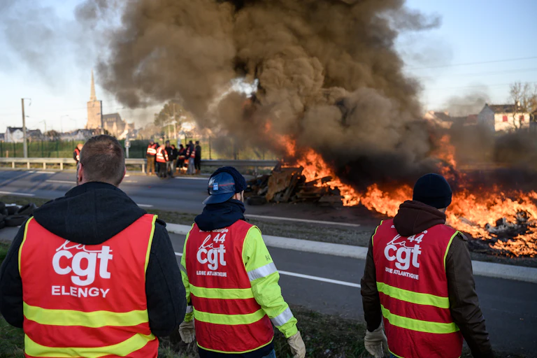 Des dizaines de syndicalistes bloquent une route avec un feu devant la raffinerie Total Energies lors d'une action appelée par la Confédération générale du travail (CGT) contre une réforme des retraites profondément impopulaire à Donges, dans l'ouest de la France, le 8 février 2023.