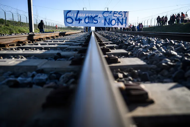 Des manifestants se tiennent sur les voies ferrées avec une banderole indiquant « 64 ans, c’est non » lors d’une action appelée par la Confédération générale du travail (CGT) pour protester contre une réforme des retraites profondément impopulaire à Donges