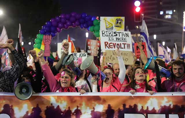 Israeli protesters shout through bullhorns and wqave anti-Netanyahu banners on the streets of Tel Aviv, March 2023.