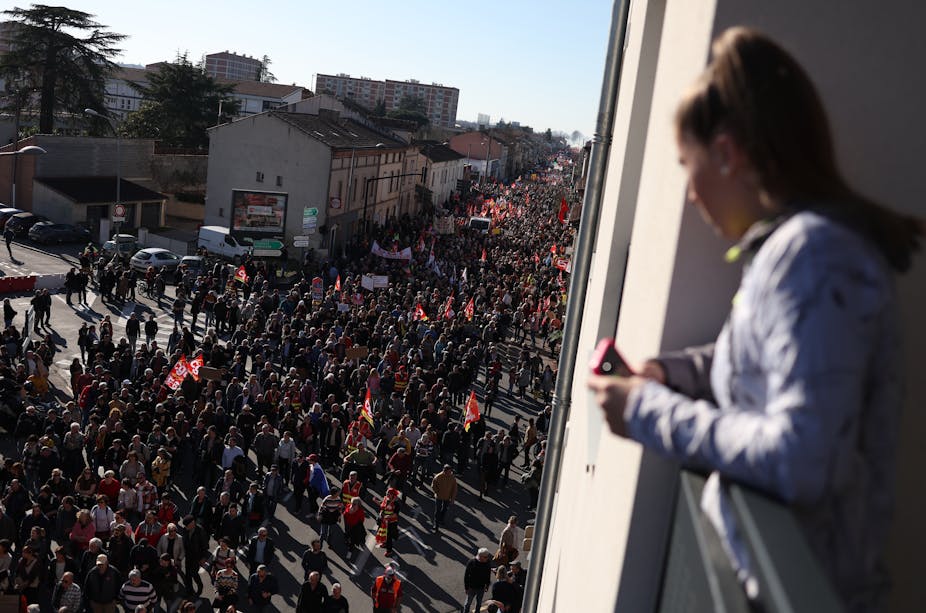 Une femme regarde de sa fenêtre des personnes participant à une manifestation au cinquième jour des rassemblements nationaux organisés depuis le début de l'année, contre une réforme des retraites profondément impopulaire, à Albi, dans le sud-ouest de la France, le 16 février 2023.