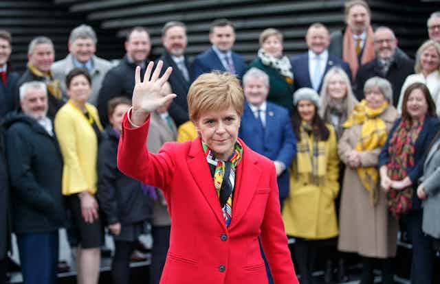 Nicola Sturgeon waving bit looking serious in front of her SNP colleagues.
