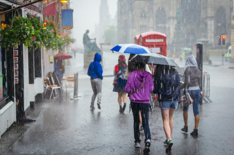 Group of girls with an umbrella walking through a city.