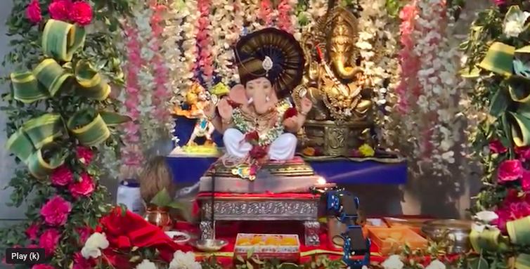 A robotic arm (below on right) is used to worship by maneuvering a candle in front of the Hindu god Ganesha.