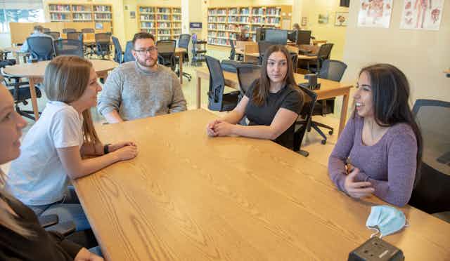 Students seen in discussion around a table with anatomy posters on the wall behind them.