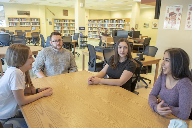Students seen in discussion around a table with anatomy posters on the wall behind them.