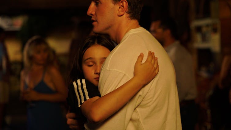 A young girl hugs her dad's chest. He wears a white tshirt.