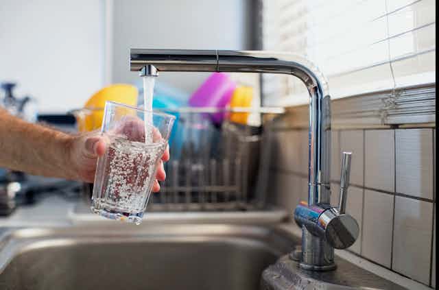 A hand holds a water glass under a flowing kitchen tap.