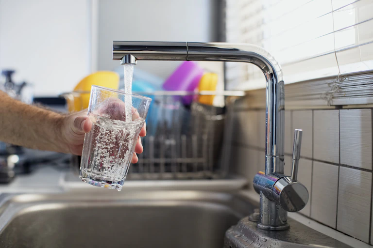 A hand holds a water glass under a flowing kitchen tap.