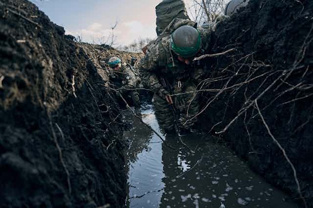 Soldiers in battle fatigues crouch in a muddy trench.
