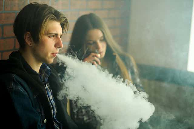 Un jeune homme et une jeune femme fument leur vapoteuse dans un espace fermé