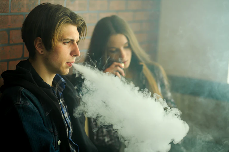 Un jeune homme et une jeune femme fument leur vapoteuse dans un espace fermé