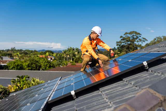 Worker installs solar panels on the roof of a suburban house