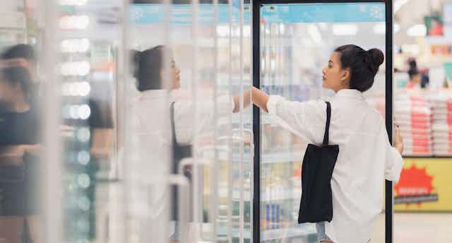 Woman opening refrigerator door in supermarket.