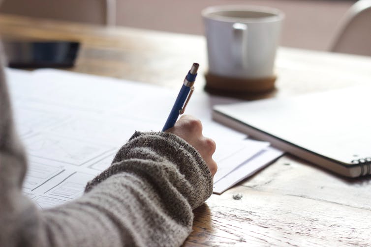 Someone writes at desk, with a tea mug.