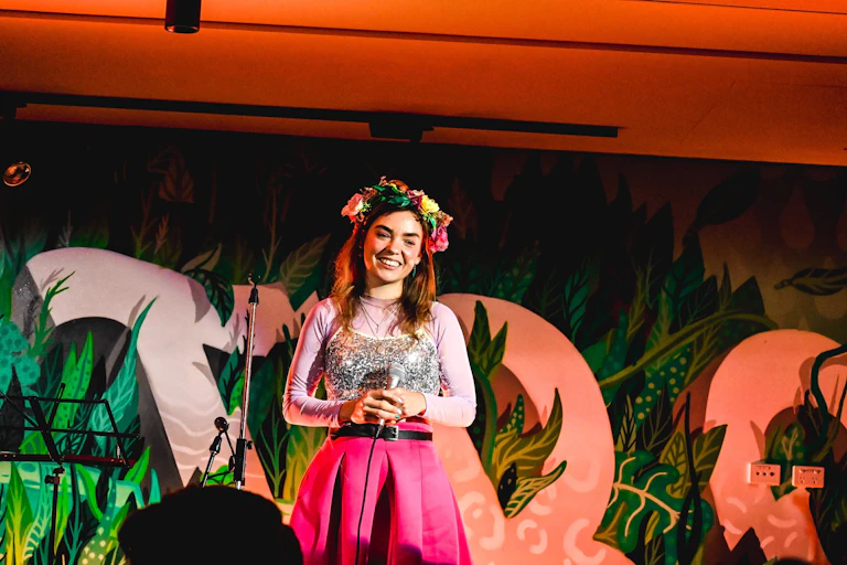 Chloe Hayden, a girl in a silver sequinned singlet over a pink top, with a pink skirt, wearing a flower crown and holding a microphone