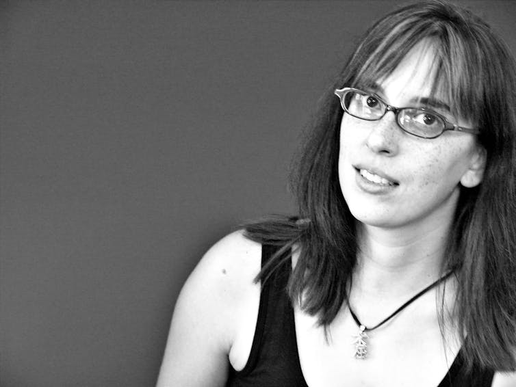 A woman with glasses in a black tank-top and a necklace, with a fringe and shoulder-length hair