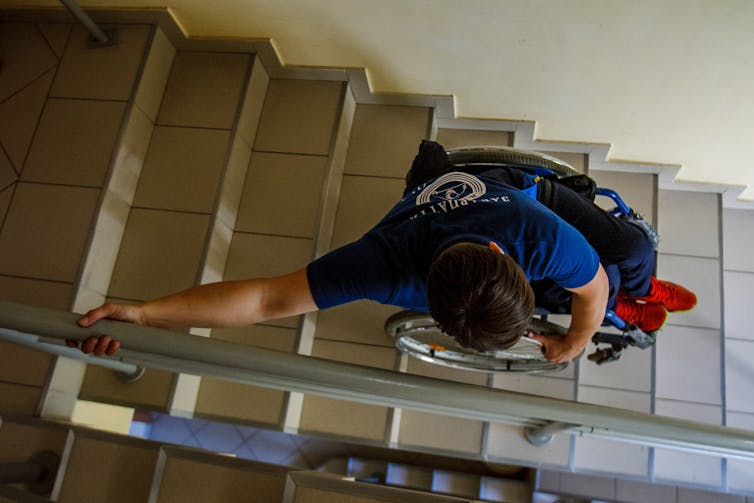 A short-haired wheelchair user impressively navigates a flight of stairs.