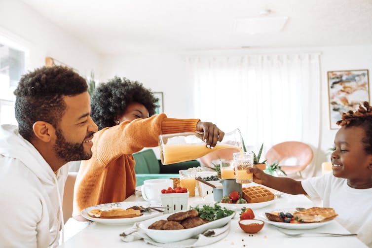 two parents and child share breakfast food at table
