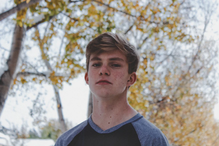 Young man standing under trees.
