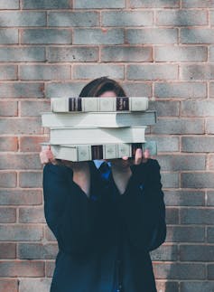 Young person holding a pile of books over their face.