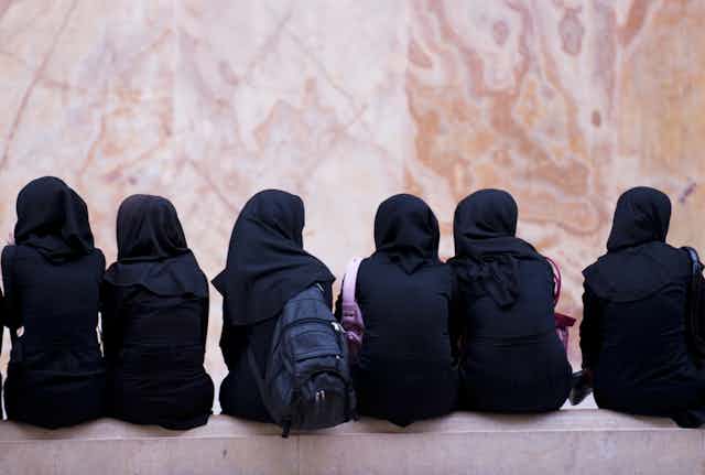 Schoolgirls wearing headscarves sitting on a bench