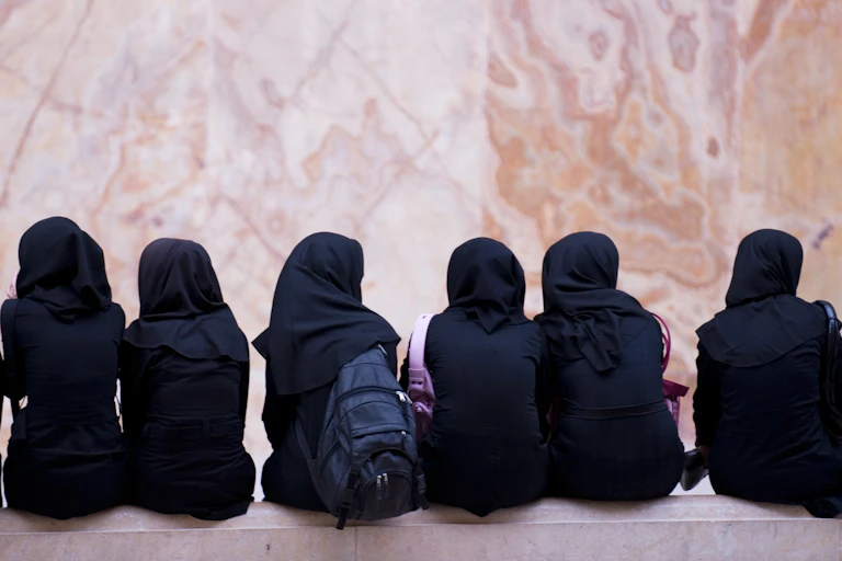 Schoolgirls wearing headscarves sitting on a bench
