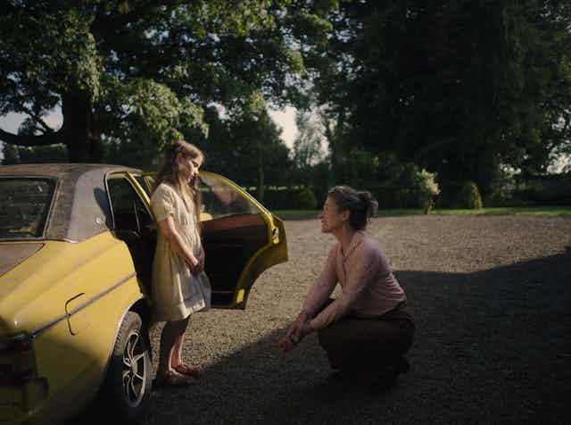 Una mujer habla con una niña delante de un coche.