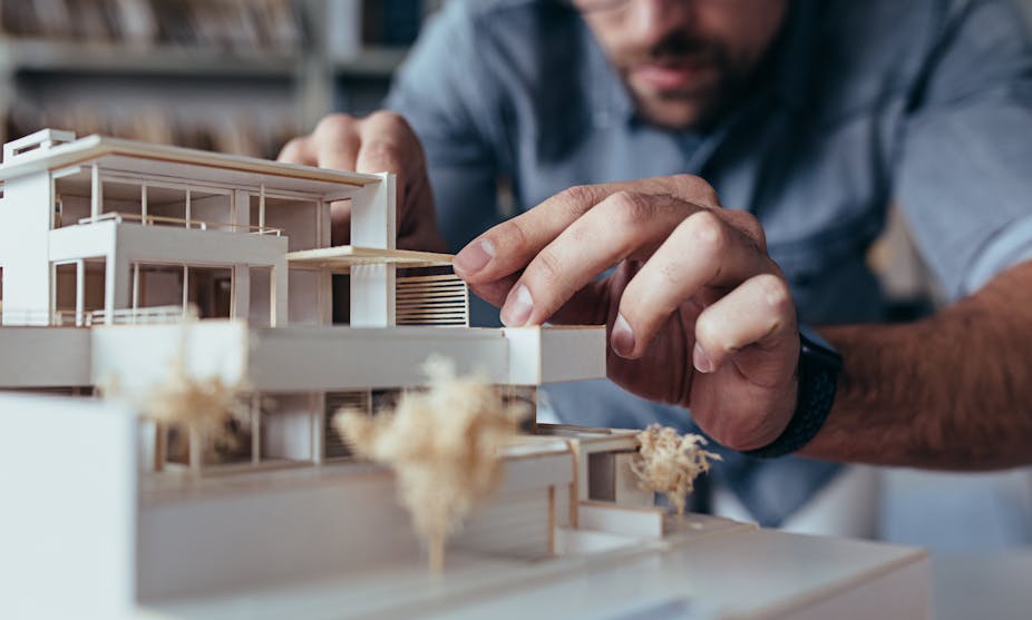 An architect working on a model of a modern looking building.