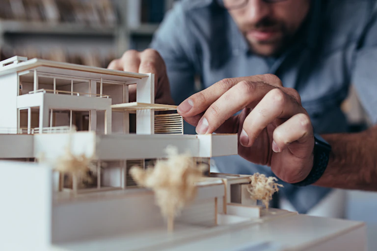 An architect working on a model of a modern looking building.