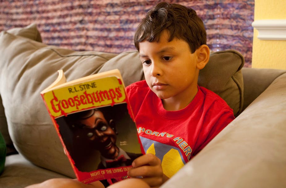 A young boy reads a copy of Goosebumps. 