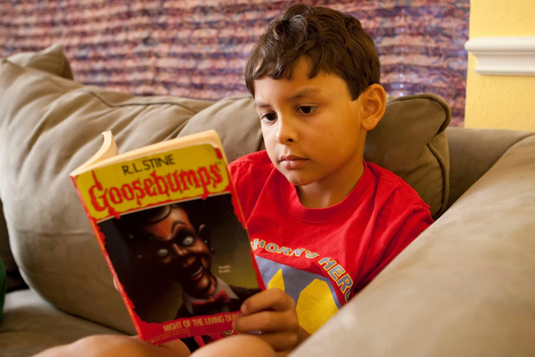 A young boy reads a copy of Goosebumps.