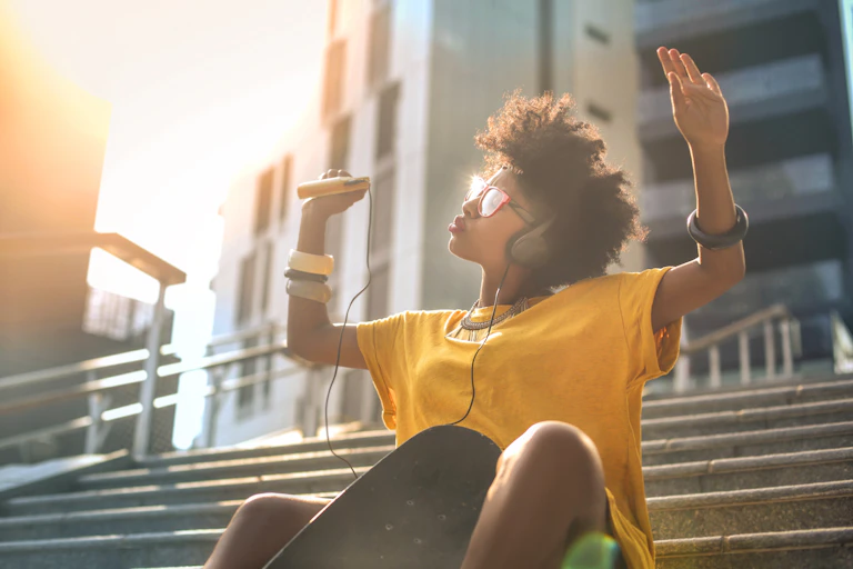 Young black woman with headphones raising her hands in enjoyment.