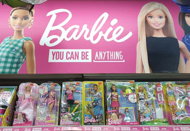 Barbie toys on store shelf under pink sign that says: "Barbie you can be anything"