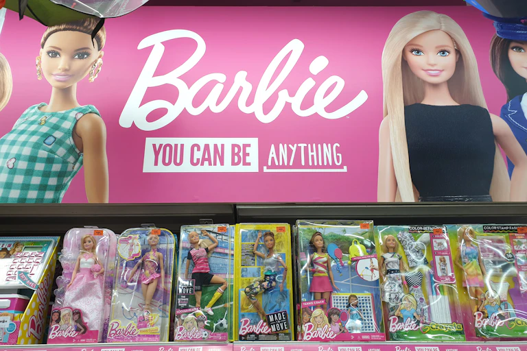 Barbie toys on store shelf under pink sign that says: "Barbie you can be anything"