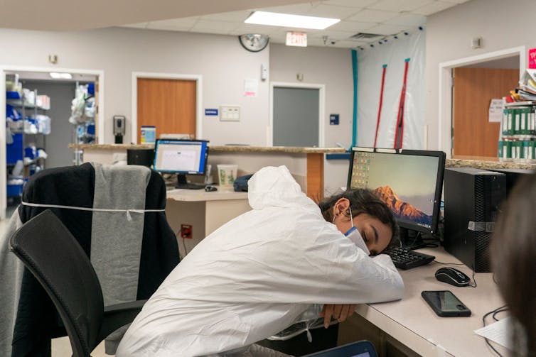 Healthcare worker sleeping at computer in nursing station.