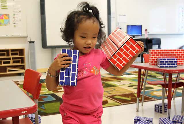 A child seen carrying cardboard bricks in a classroom.