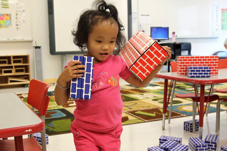 A child seen carrying cardboard bricks in a classroom.