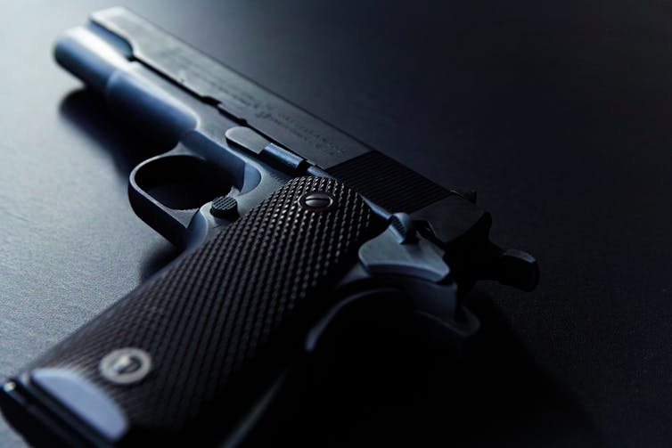 A black handgun lays flat on a black tabletop with light illuminating the tip of the gun.