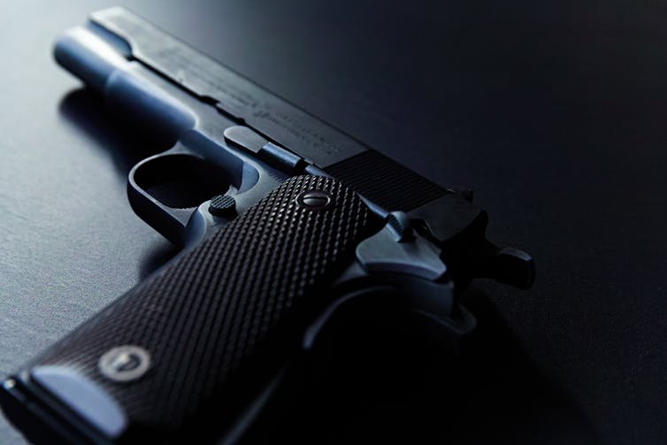 A black handgun lays flat on a black tabletop with light illuminating the tip of the gun. 