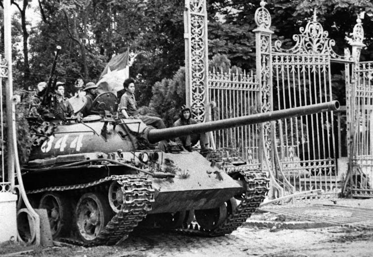 A black and white photo of a tank driving through a destroyed gate.