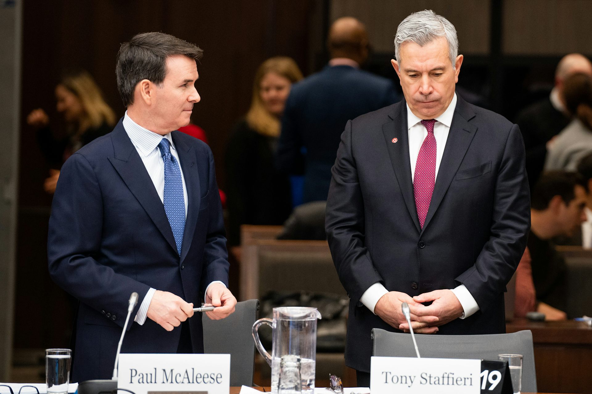 Two men in suits stand before a table with name cards sitting on it