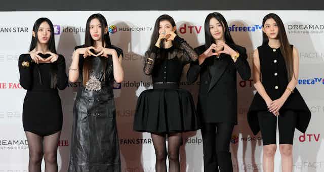 Five young women wearing black outfits pose for a photo.