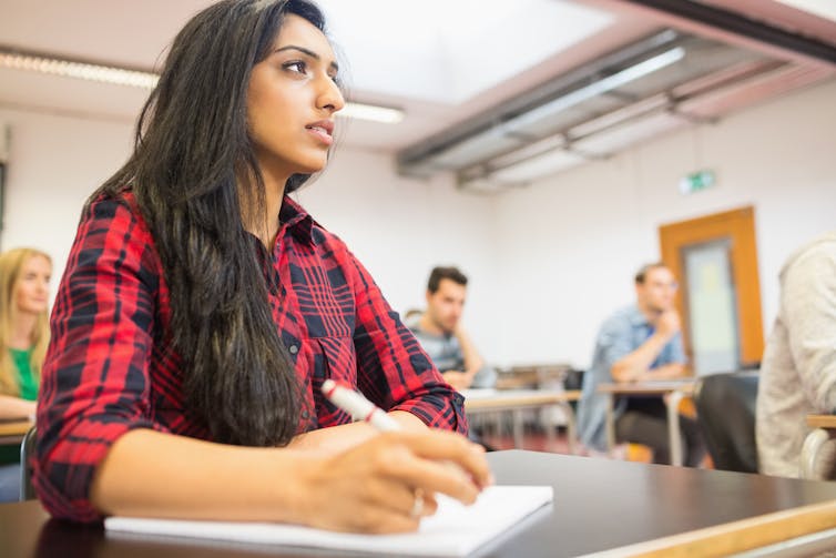 A young woman listens to a teacher in a classroom.