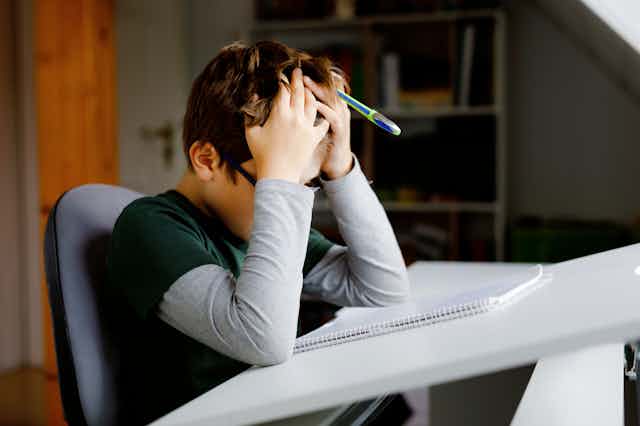A child puts their head in their hands, while sitting at a desk.