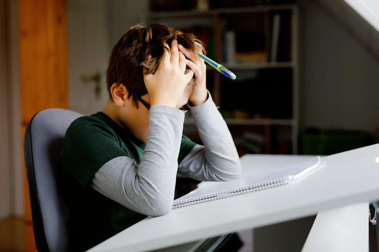 A child puts their head in their hands, while sitting at a desk.