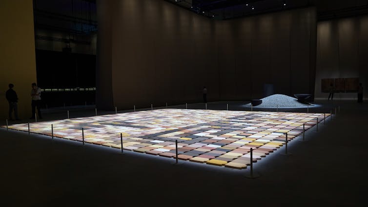 Tablet shaped forms are placed together, each a different shade of black, white, browns and yellows, to form a vast mosaic.