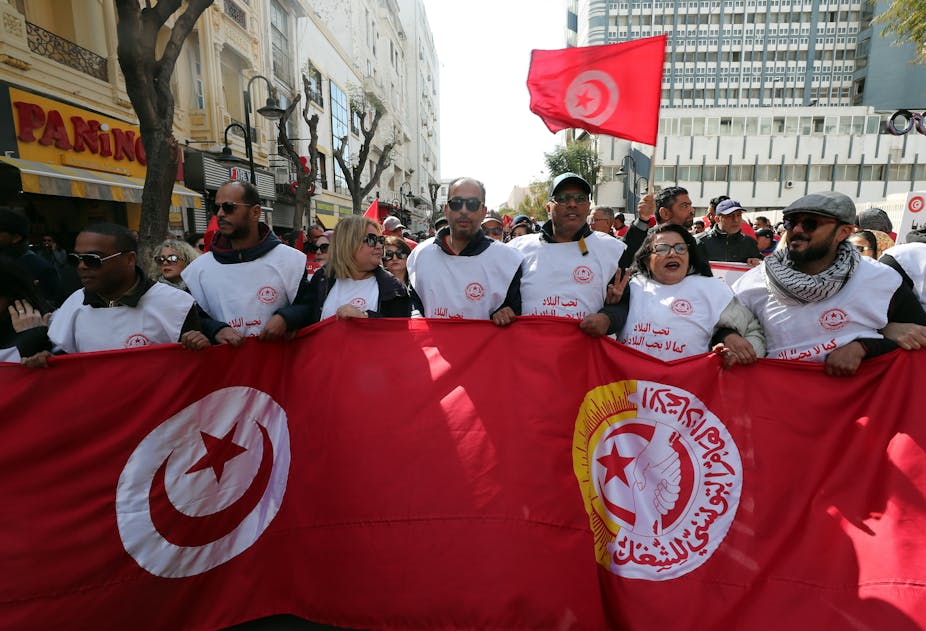 Personas vestidas con chaquetas blancas y sosteniendo una gran bandera.