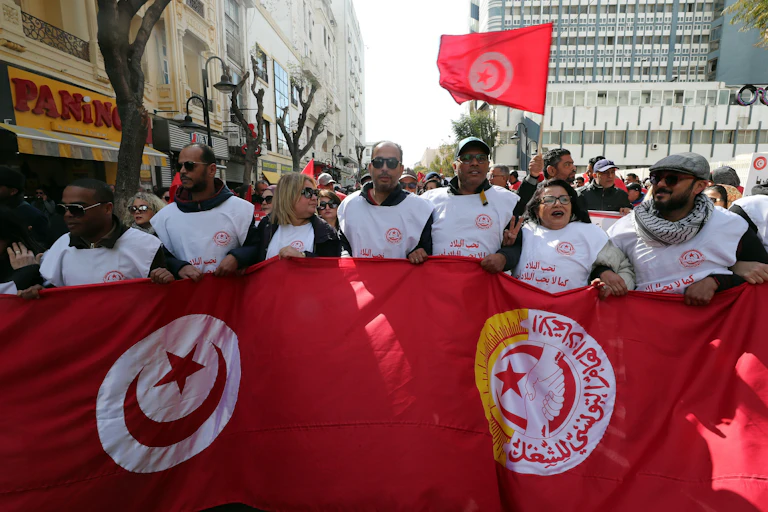 People wearing white jackets and holding a large flag.