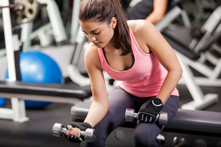 A woman performs a bicep curl in the gym using silver dumbbells.