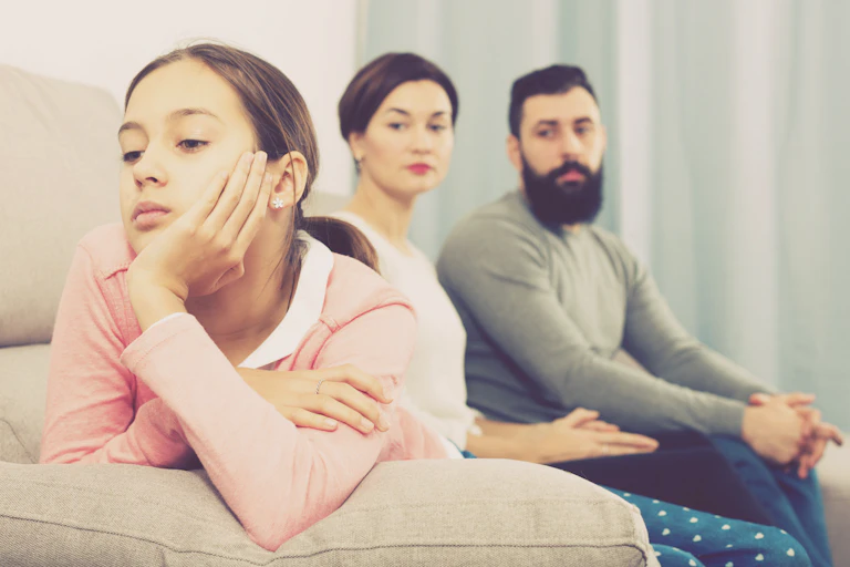 Child looking away from parents sat on sofa